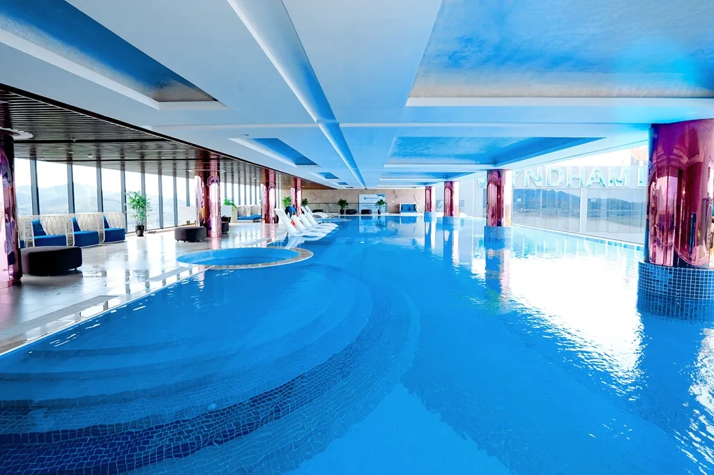 Sky Onsen Pool ở Lynntimes Thanh Thủy với bể bơi dài nước xanh, bể sục tròn, ghế nằm trắng và vách kính nhìn ra núi