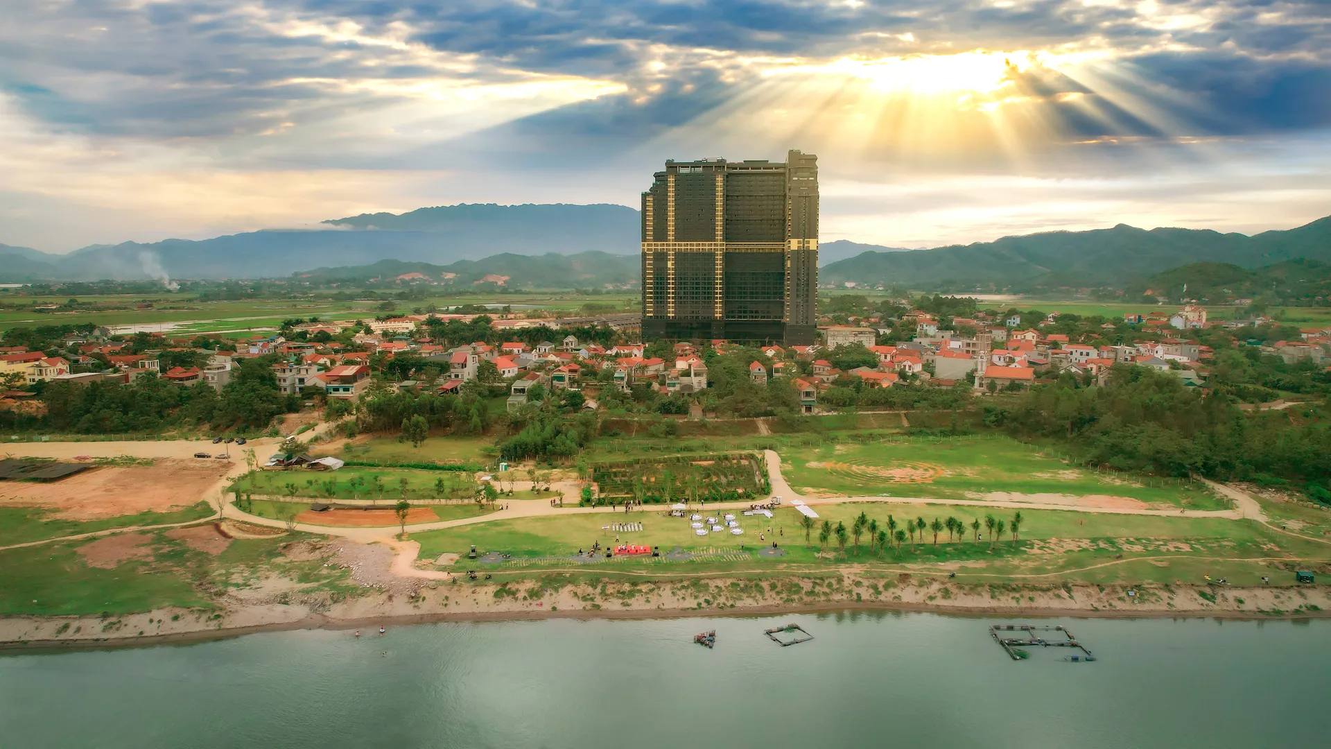 Toàn cảnh tòa khách sạn Lynntimes Thanh Thủy giữa làng quê, phía trước là bãi cỏ và mặt sông Đà, núi xa phía sau lúc hoàng hôn