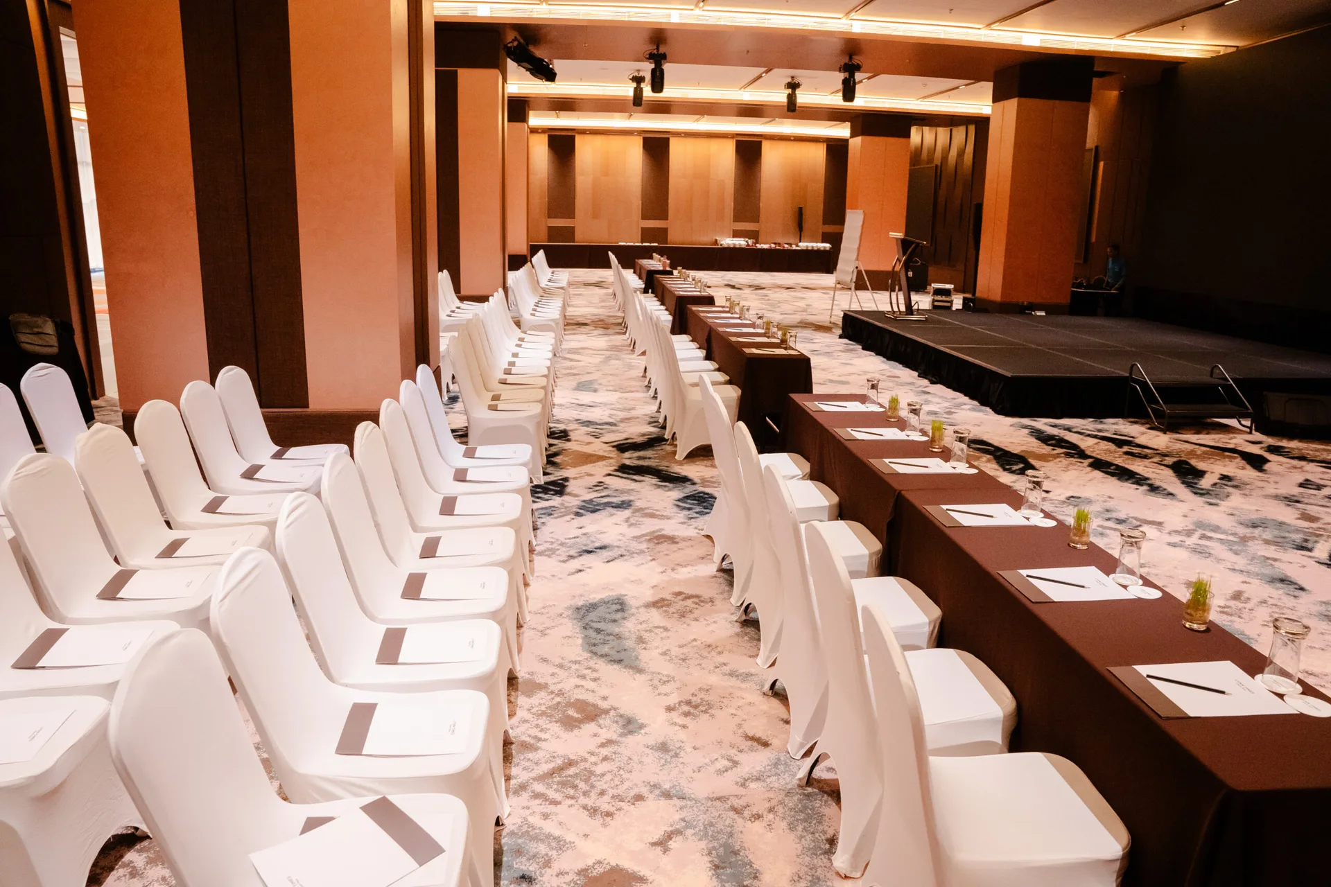 Trung tâm hội nghị Lynntimes Thanh Thủy kê ghế bọc trắng kiểu rạp hát và dãy bàn phủ khăn nâu cạnh sân khấu