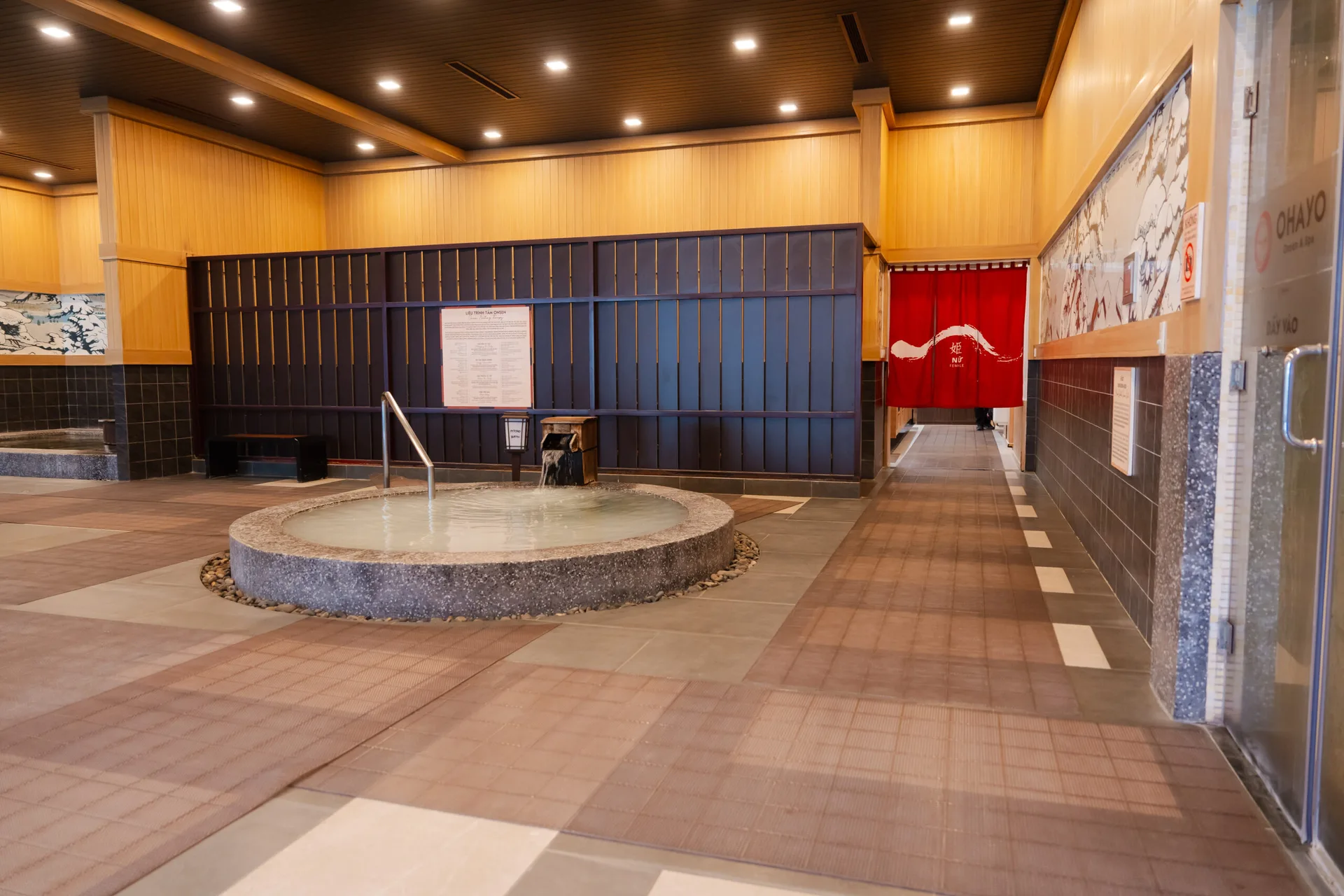 Khu tắm Nhật Japanese Onsen trong nhà, bể tròn nước trắng đục có vòi gỗ, rèm đỏ khu nữ phía sau