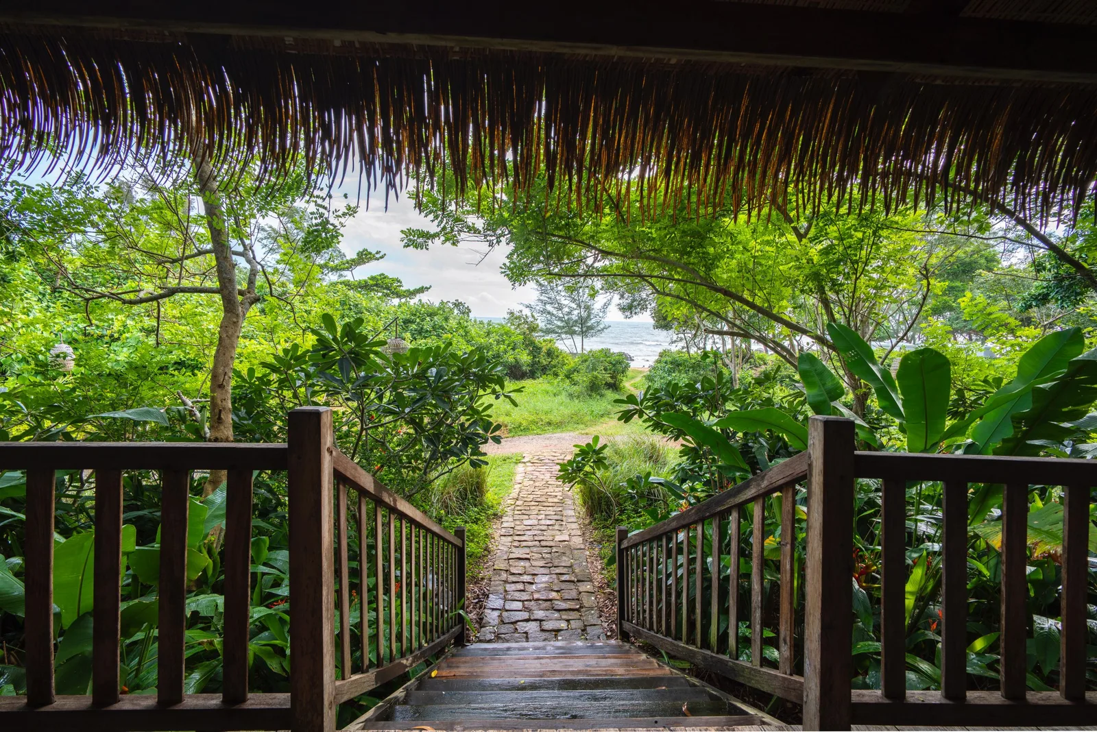 Lối đi lát đá từ hiên bungalow mái lá của Mango Bay xuyên qua vườn cây xanh ra phía biển