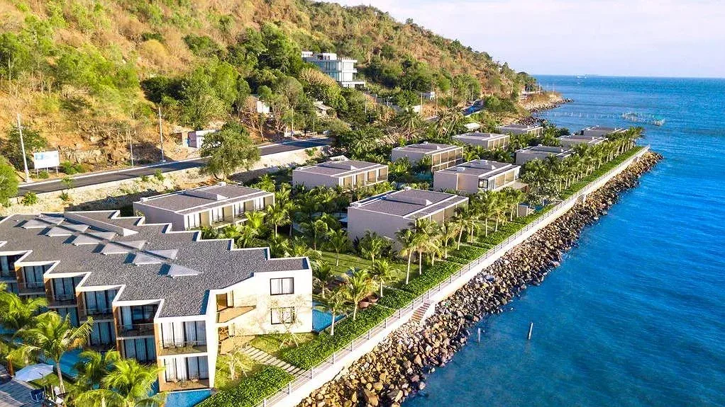 Flycam Marina Bay Vũng Tàu Resort & Spa: dãy villa mái xám giữa hàng dừa, kè đá sát mặt biển xanh và sườn Núi Lớn phía sau