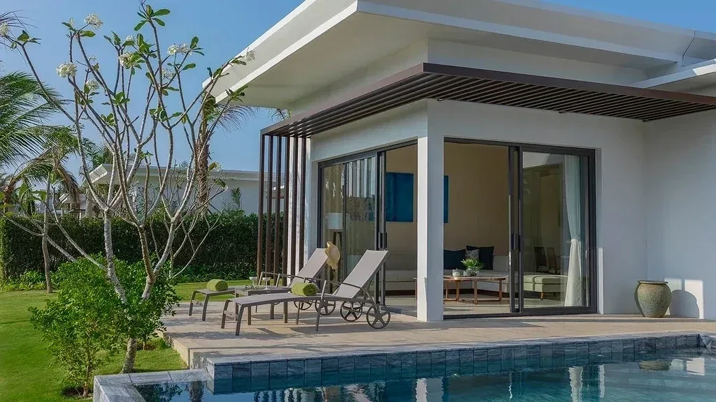 Góc The Level Beach Villa 2 Phòng Ngủ ở Melia Hồ Tràm: ghế nằm trên sàn gỗ cạnh hồ bơi riêng, cửa kính mở vào phòng khách