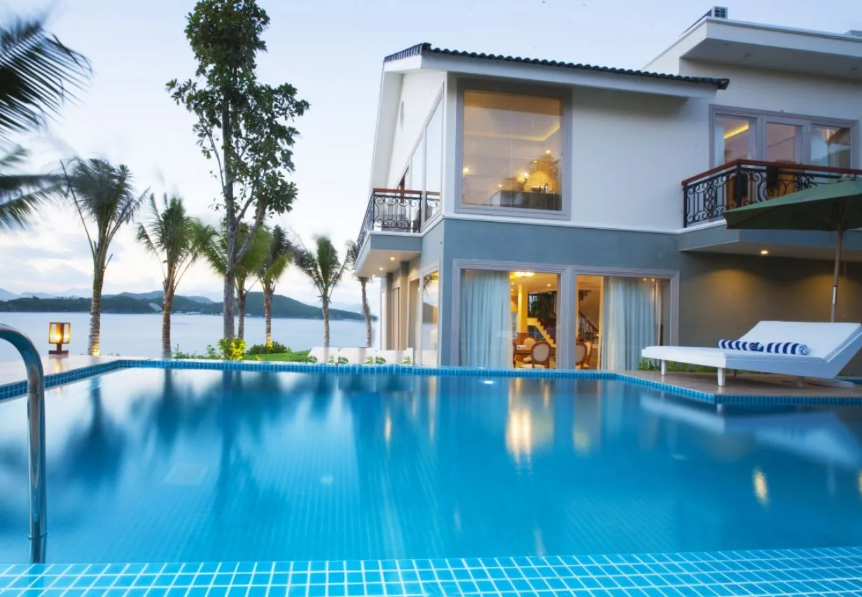 Biệt thự hai tầng tại MerPerle Hòn Tằm Resort, hồ bơi vô cực riêng lát gạch xanh trước hiên, ghế tắm nắng trắng và vịnh biển phía xa