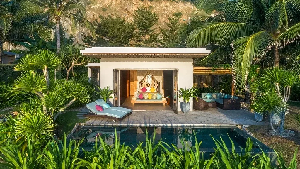 Cliff Villa tại Mia Resort Nha Trang, nhà mái bằng tường trắng mở cửa ra sân đá, hồ bơi riêng phía trước, ghế tắm nắng và vách núi phía sau