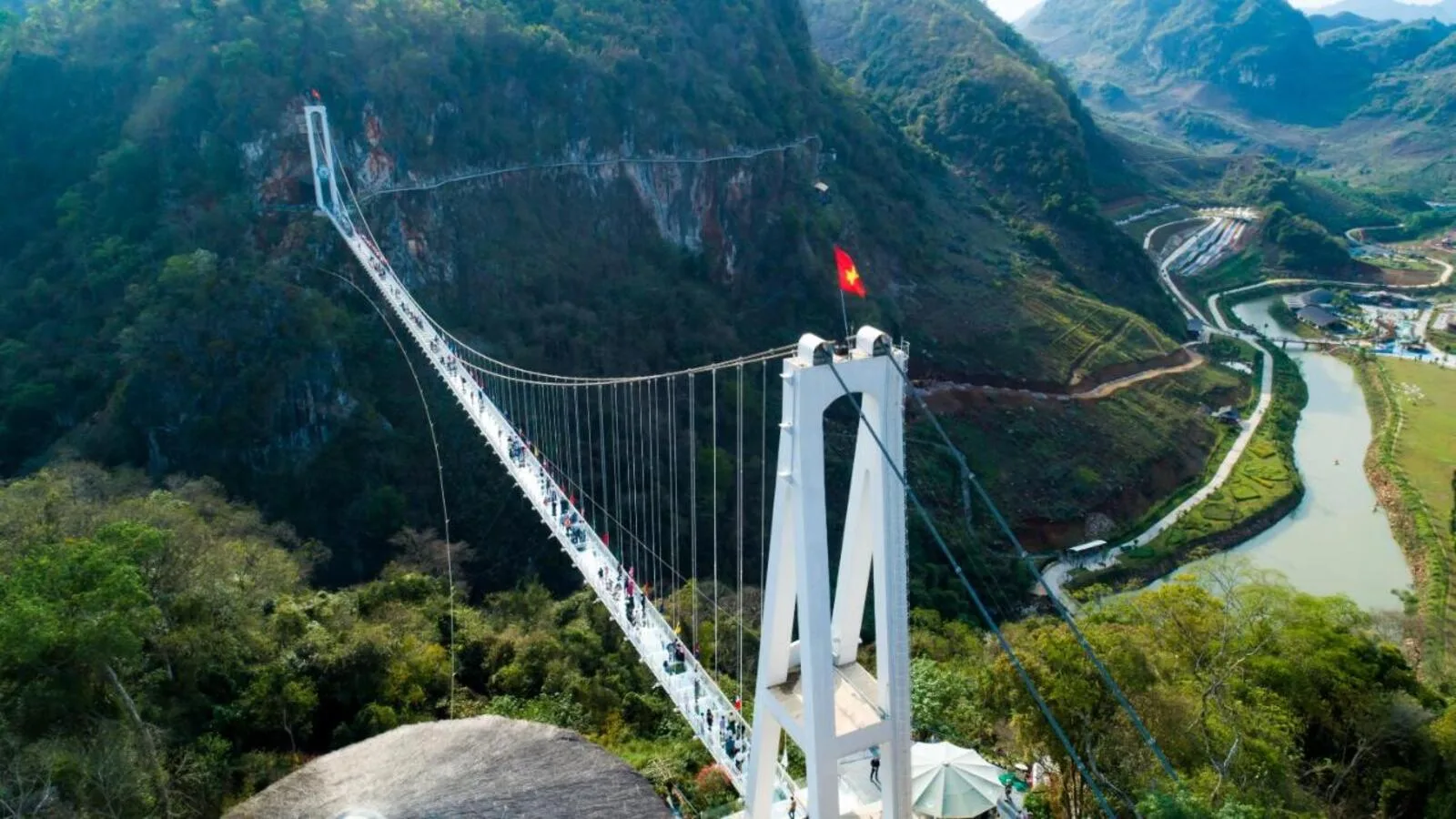 Cầu kính Bạch Long trắng vắt qua vách núi xanh, bên dưới là thung lũng có sông uốn khúc tại quần thể Mộc Châu Island