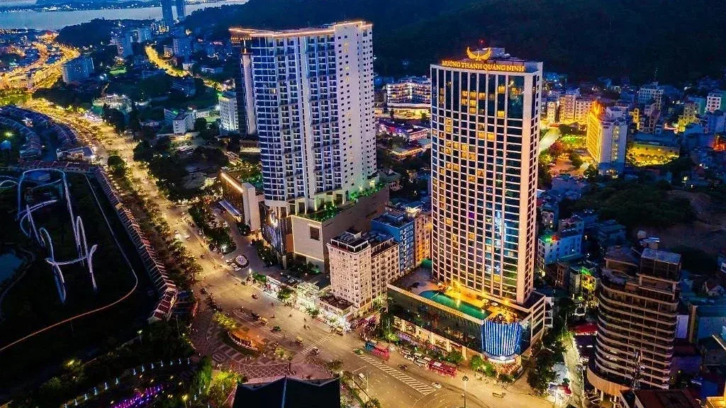 Mường Thanh Luxury Quảng Ninh về đêm, toà tháp sáng đèn với bể bơi trên khối đế, bên cạnh đại lộ và phố Bãi Cháy