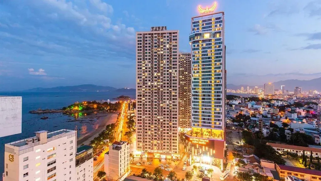 Hai tòa tháp Mường Thanh Luxury Viễn Triều lên đèn lúc chạng vạng, bên trái là đường ven biển và mỏm đá Hòn Chồng