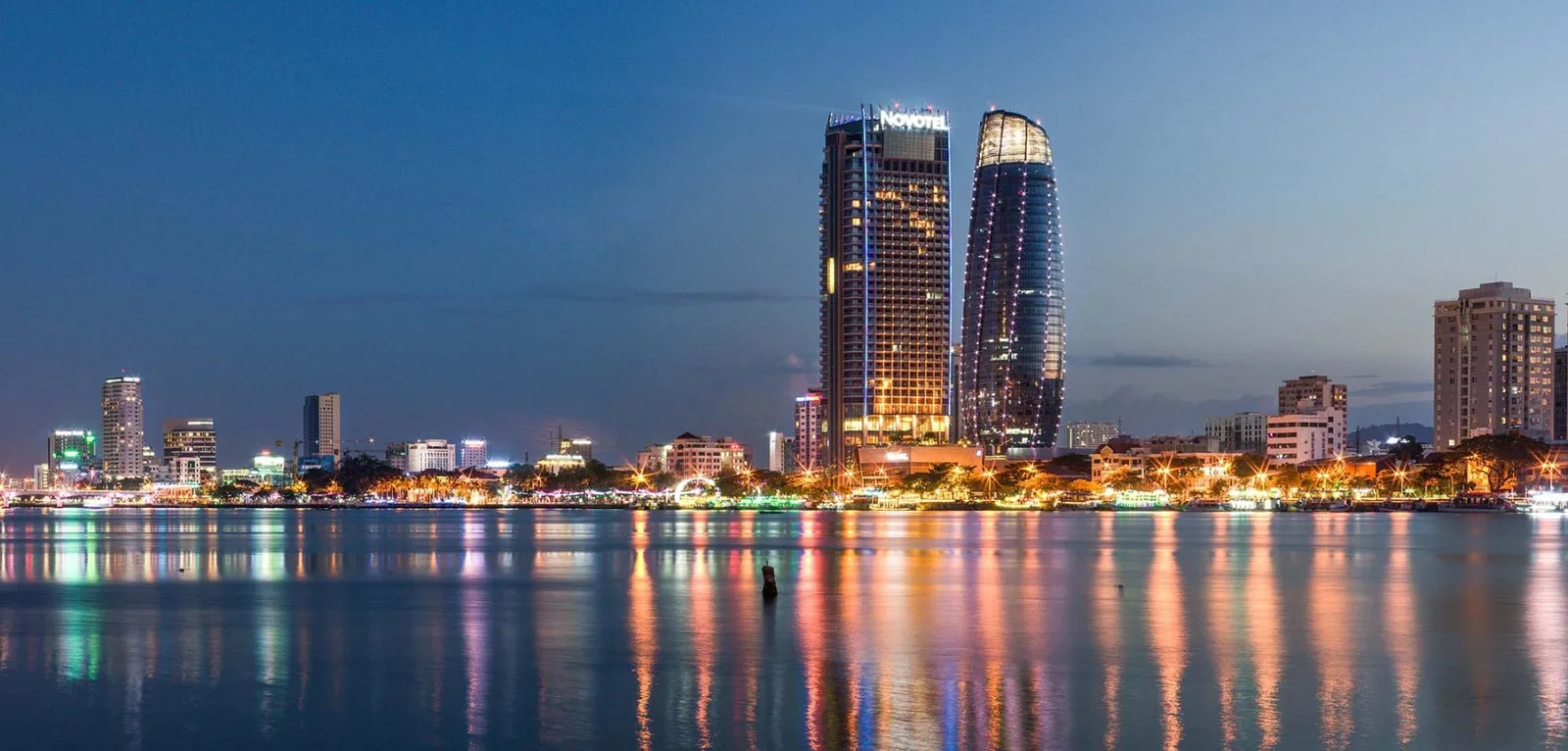 Tòa tháp Novotel Danang Premier Han River lên đèn bên bờ sông Hàn, mặt nước phản chiếu ánh đèn thành phố