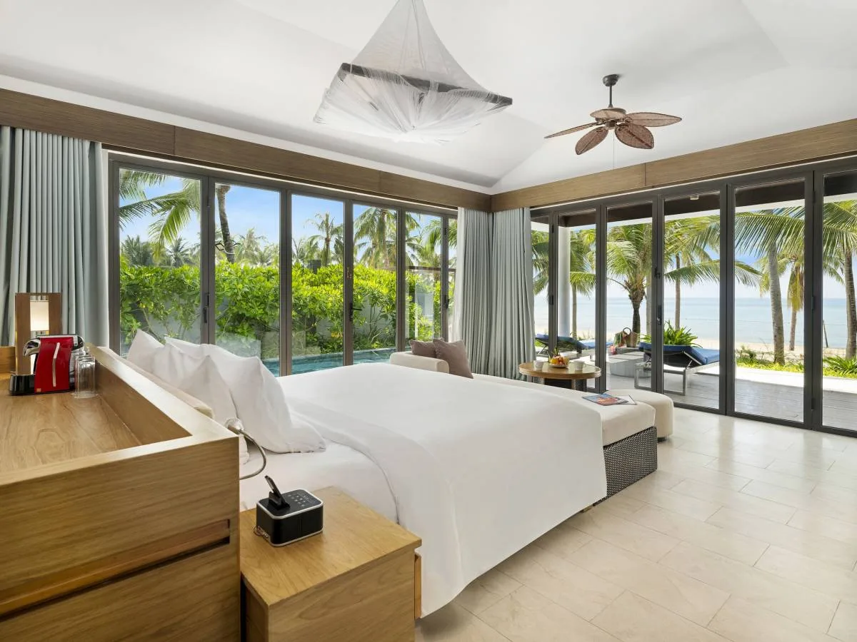 Phòng ngủ Deluxe Beachfront Bungalow - Hồ Bơi Riêng tại Novotel Phu Quoc Resort: giường trắng, cửa kính trượt mở ra hồ bơi riêng và bãi cát, biển xanh phía sau hàng dừa