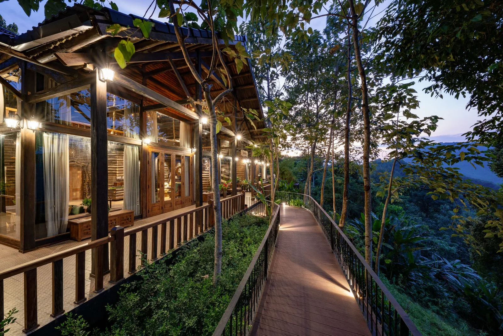 Villa gỗ vách kính của P'apiu Resort lên đèn lúc chạng vạng, lối đi gỗ men theo sườn đồi nhìn ra thung lũng