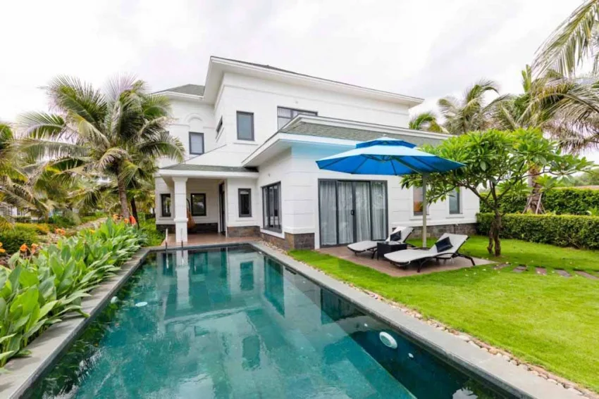 Garden Pool Villa 3 phòng ngủ ở Parami Resort Ho Tram: căn nhà hai tầng tường trắng, hồ bơi riêng hình chữ nhật, ghế nằm và dù xanh trên bãi cỏ