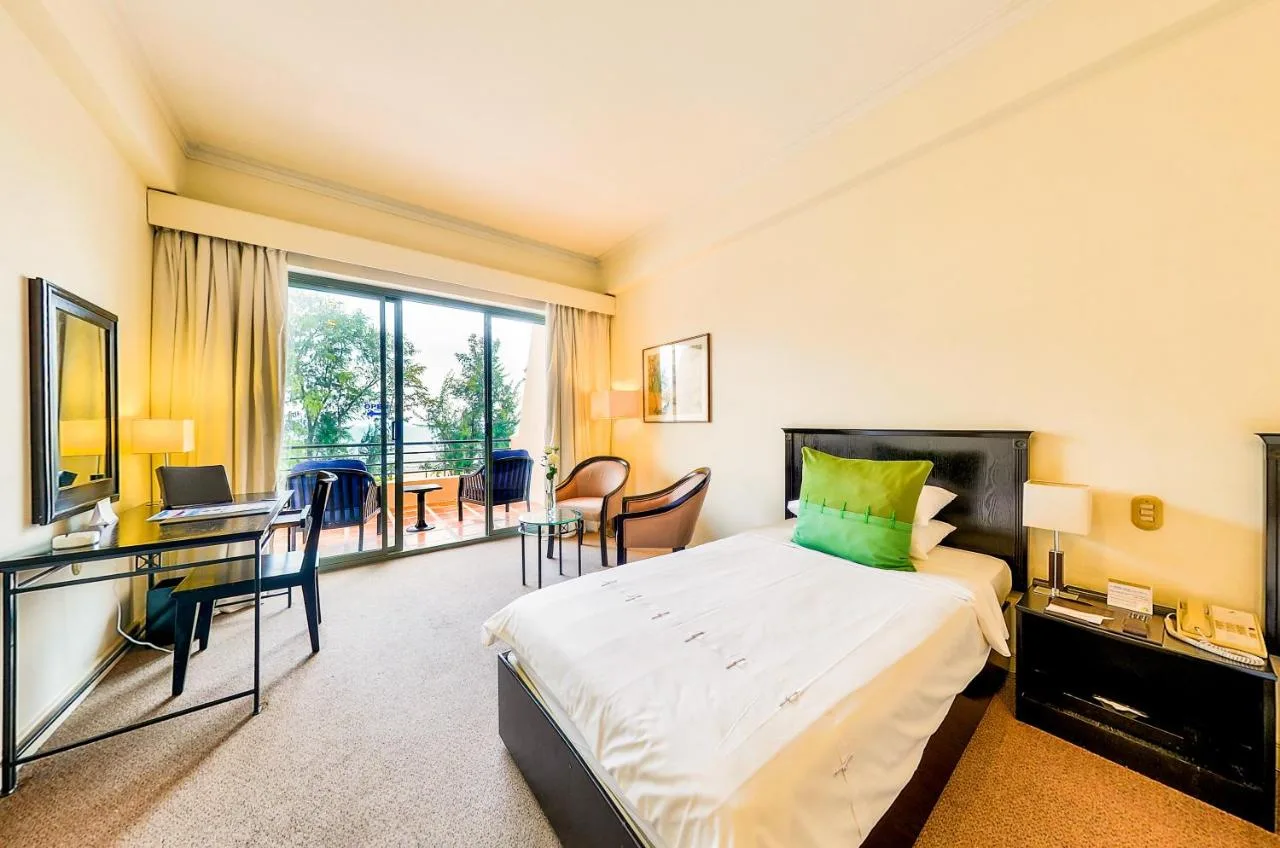 Phòng Superior của Phan Thiet Ocean Dunes Resort với giường trắng gối xanh lá, bàn làm việc và cửa kính mở ra ban công có ghế ngồi