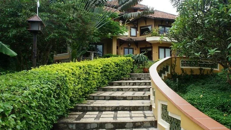 Bậc thang đá giữa hàng rào cây xanh dẫn lên dãy nhà mái ngói đỏ tường vàng của Poshanu Resort