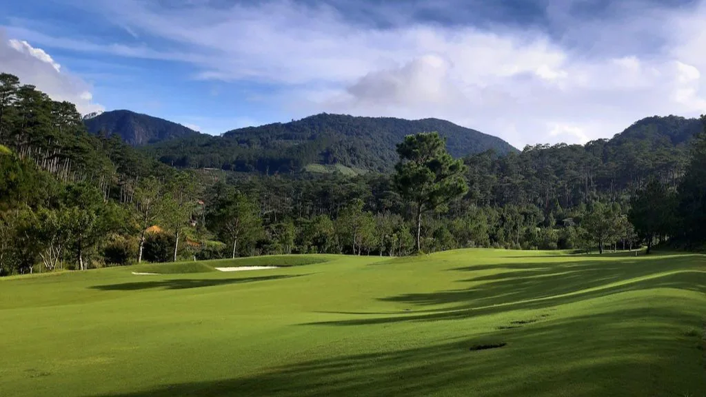 Sân golf cỏ xanh giữa rừng thông và dãy núi dưới trời nhiều mây tại Sacom Tuyền Lâm Resort Đà Lạt