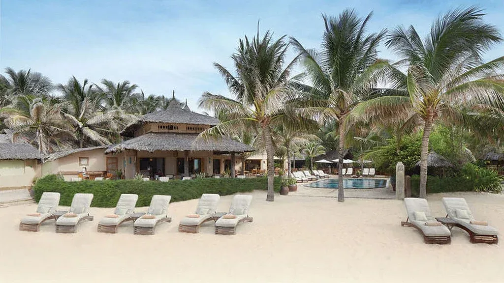 Bãi cát trước Sailing Club Resort Mũi Né, ghế nằm trắng, nhà mái tranh và hồ bơi dưới hàng dừa