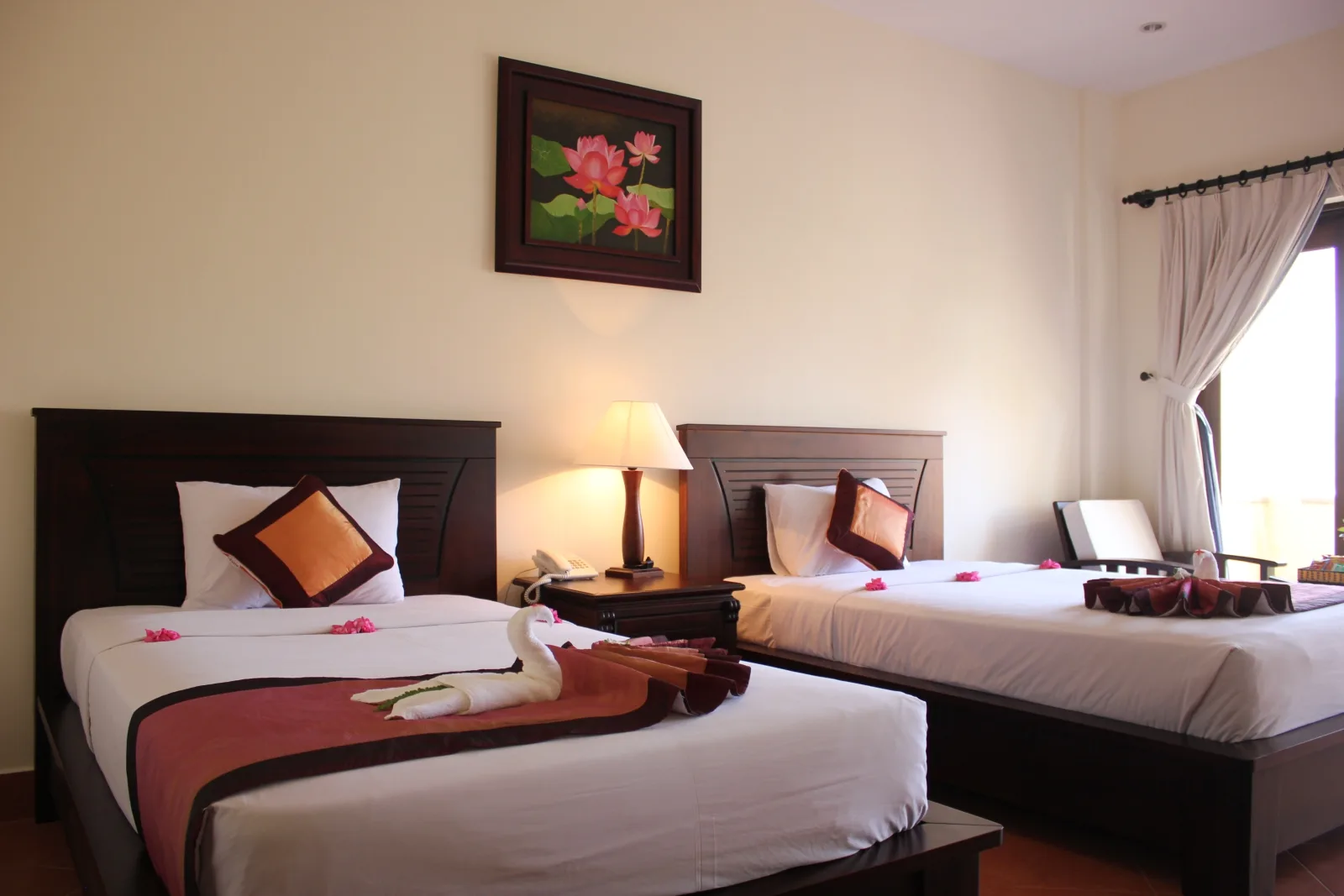 Phòng Deluxe Garden View của Sea Lion Beach Resort & Spa với hai giường đơn trải khăn đỏ nâu, tranh hoa sen treo giữa và cửa sổ rèm trắng