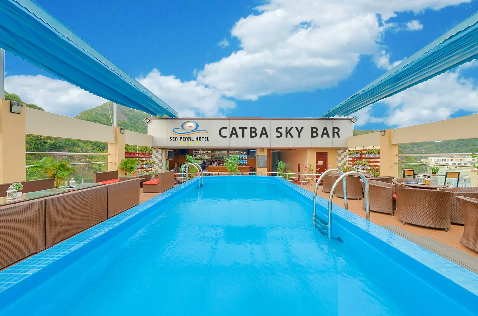 Bể bơi trên tầng thượng của Sea Pearl Cát Bà Hotel, cuối bể là quầy Catba Sky Bar, hai bên là ghế mây và đồi xanh