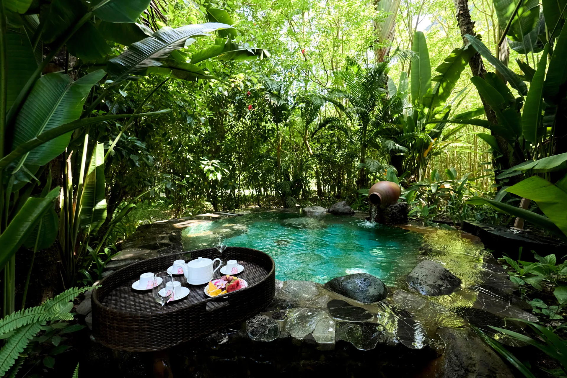 Bể khoáng ngoài trời nước xanh ngọc giữa rừng chuối và tre, vòi nước chảy từ chum gốm tại Serena Resort Kim Bôi