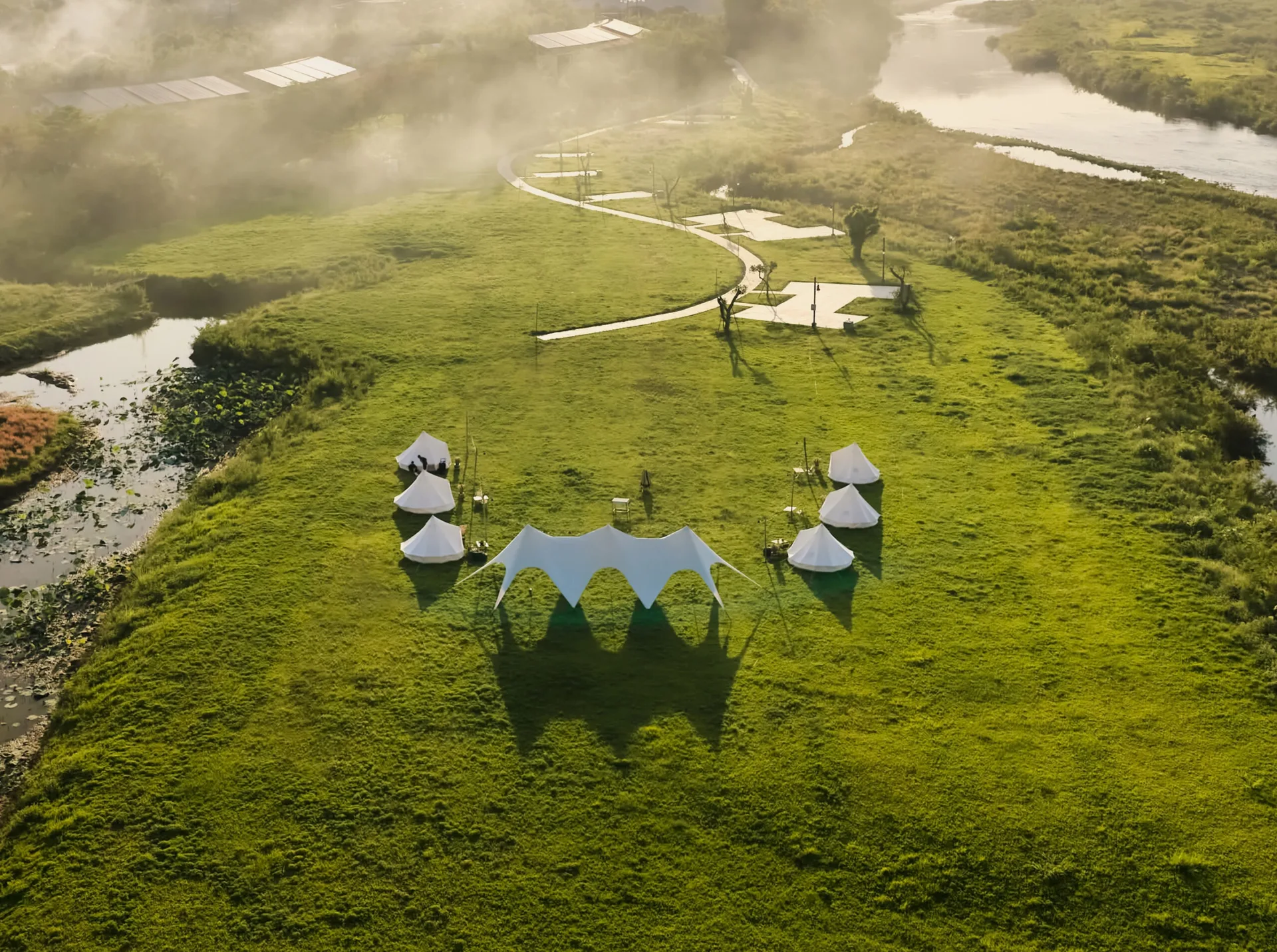 Khu cắm trại trên bãi cỏ ven sông Bôi ở Serena Resort Kim Bôi với sáu lều chuông trắng và tăng che lớn trong sương sớm