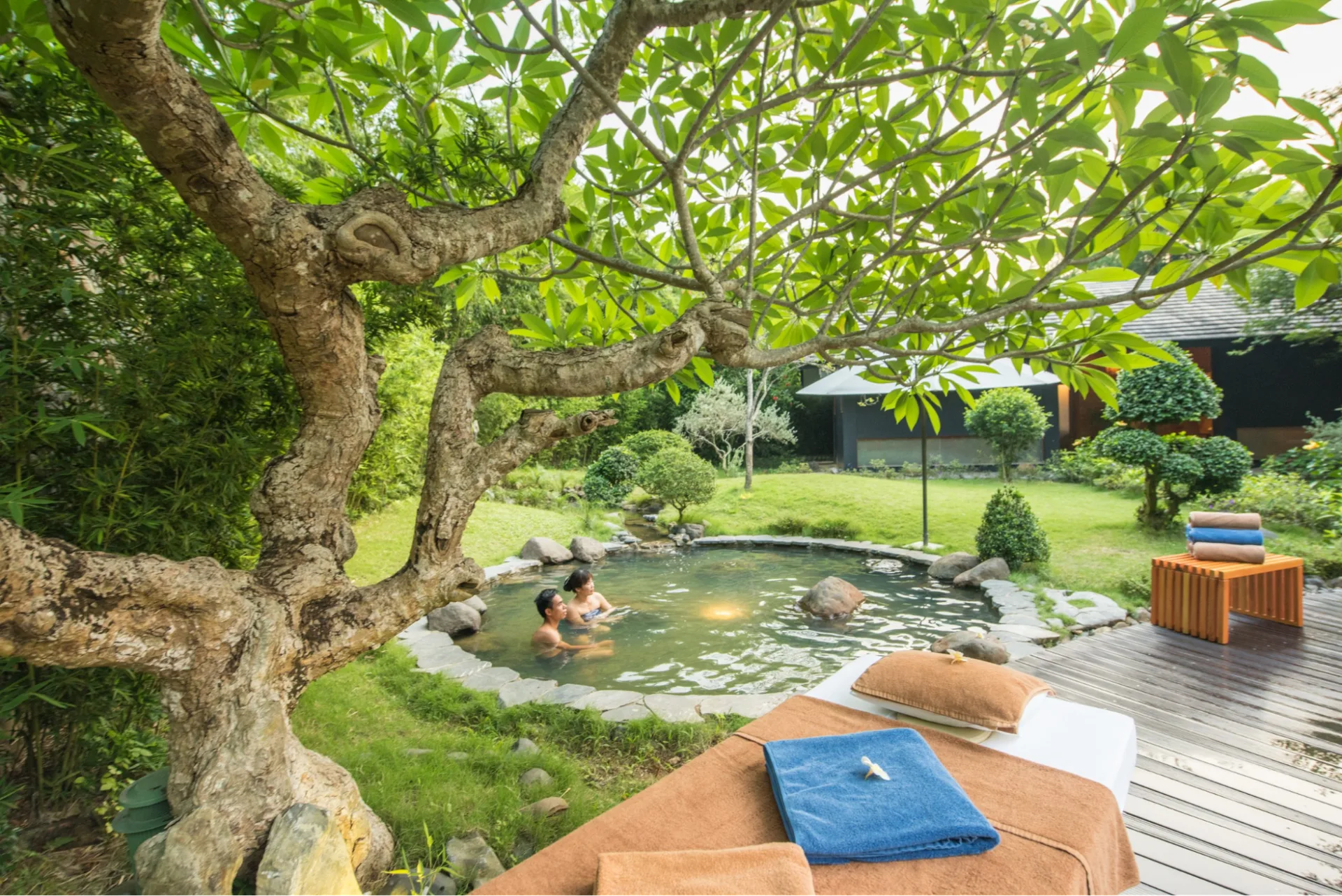 Khách ngâm trong bể onsen viền đá dưới gốc cây đại tại khu Onsen kiểu Nhật của Serena Resort Kim Bôi