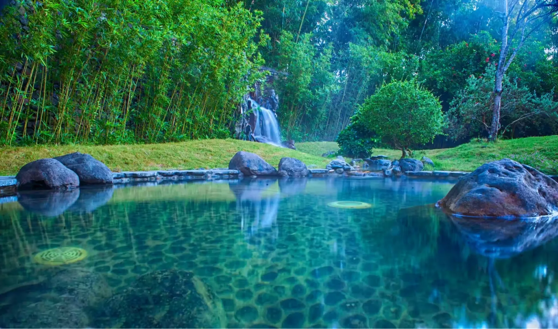 Bể khoáng ngoài trời nước trong xanh viền đá tảng, thác nước nhỏ và rặng tre trong sương sớm ở khu Onsen kiểu Nhật, Serena Resort Kim Bôi