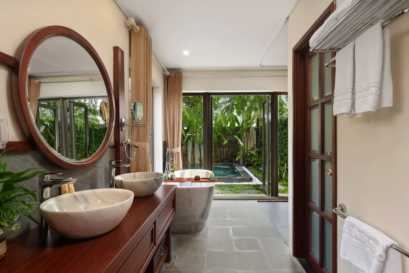 Phòng tắm Suite King Hướng Sông tại Silk Sense Hoi An River Resort, bồn đá cẩm thạch trắng xám nhìn ra khoảng vườn riêng có bể ngâm