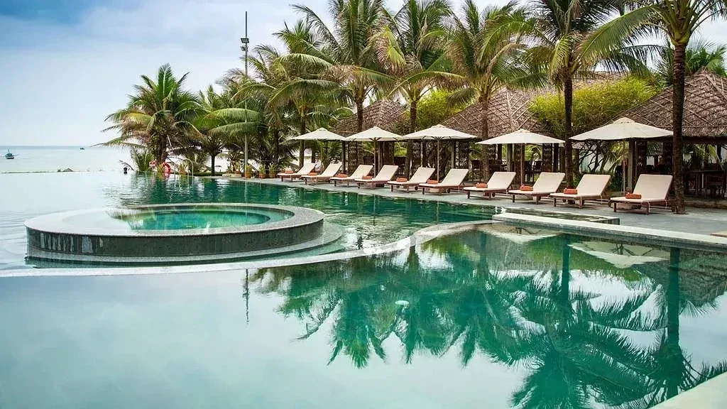 Bể bơi vô cực của Sonata Resort & Spa Phan Thiết có bồn sục tròn, hàng ghế tắm nắng dưới rặng dừa và chòi mái lá nhìn ra biển