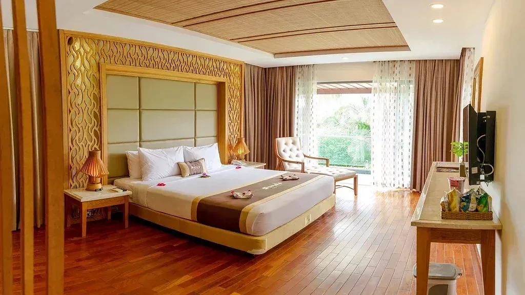 Phòng Deluxe Hướng Biển của Sonata Resort & Spa Phan Thiết với giường King, sàn gỗ, đầu giường ốp khung gỗ chạm và cửa kính mở ra vườn cây