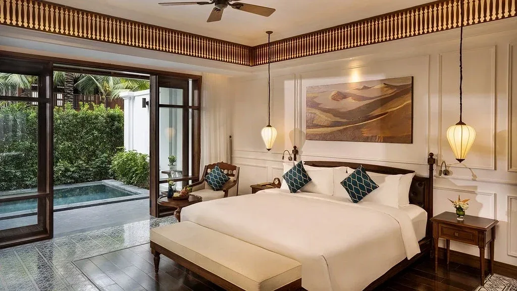 Phòng ngủ Private Pool Suite ở The Anam Mui Ne, cửa gỗ mở ra hồ bơi riêng và hàng cây xanh