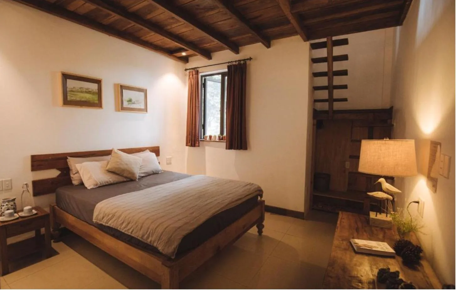 Phòng Gia đình gác lửng tại TOKI Boutique Hotel Măng Đen với giường gỗ, trần dầm gỗ, cầu thang gỗ dẫn lên gác và đèn bàn vàng ấm
