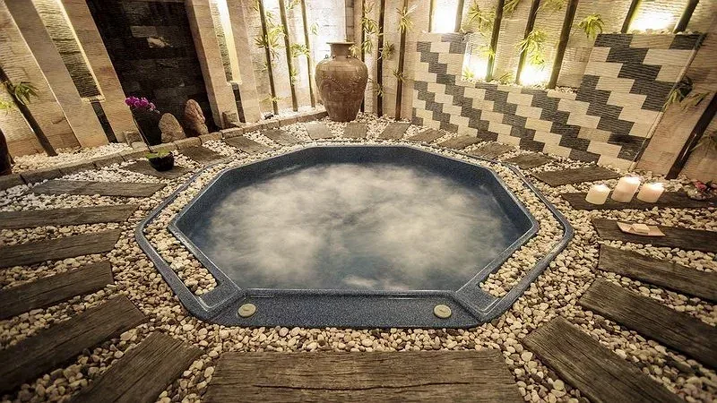 Bể ngâm nước nóng bốc hơi giữa nền sỏi và lối gỗ trong khu spa của TTC Hotel Premium Ngọc Lan Đà Lạt