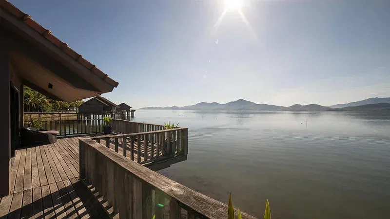 Sàn gỗ Water Villa tại Vedana Lagoon Resort & Spa vươn ra mặt đầm phẳng lặng, dãy núi xa và các villa trên cọc phía sau