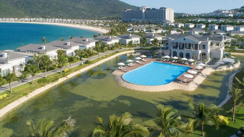 Hồ bơi lớn giữa hồ cảnh quan tại Vinpearl Golf Land Resort & Villas Nha Trang, phía sau là dãy biệt thự mái xám và bãi biển