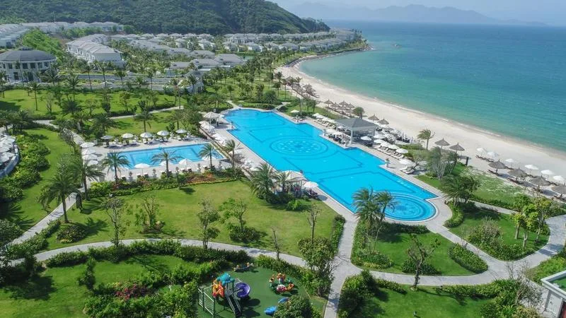 Toàn cảnh Vinpearl Golf Land Resort & Villas Nha Trang từ trên cao: bể bơi lớn giữa vườn cỏ, bãi cát trắng, dãy biệt thự và sân chơi trẻ em