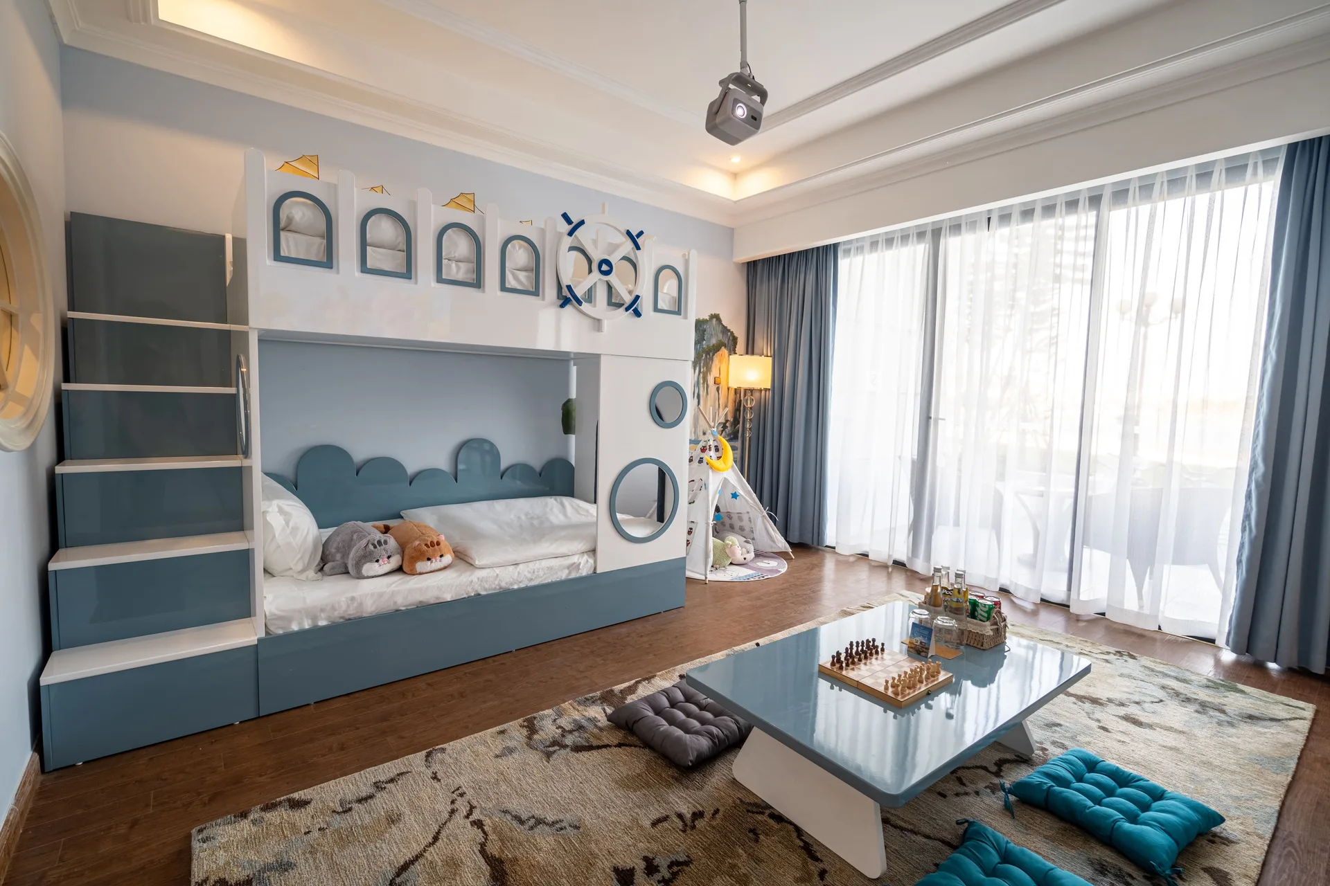 Phòng trẻ em trong Family Suite tại Vinpearl Resort & Spa Hạ Long với giường tầng hình lâu đài xanh trắng, lều vải, bàn thấp có bàn cờ và máy chiếu trên trần