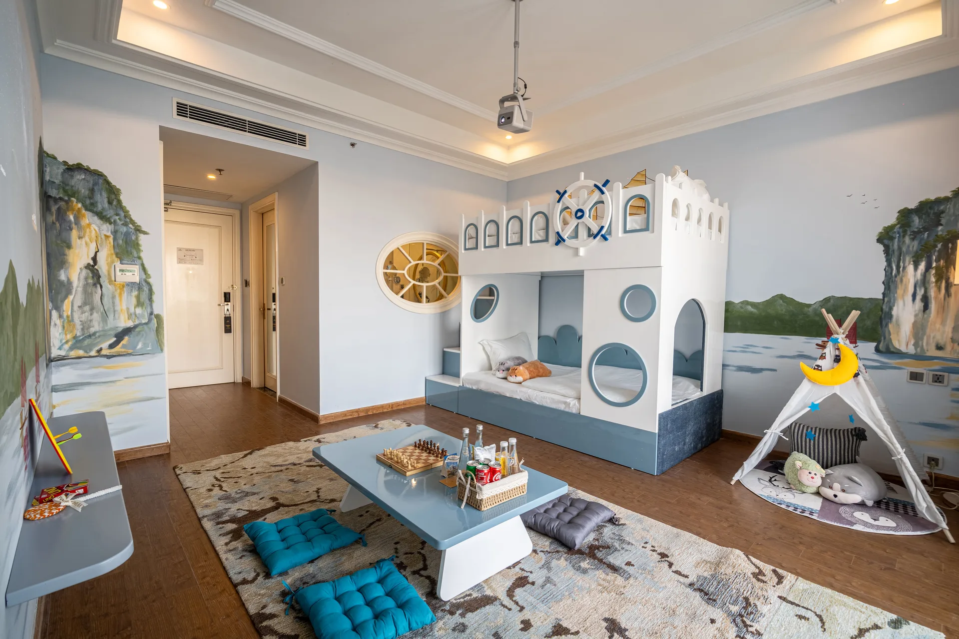 Phòng trẻ em của Family Suite với giường tầng hình lâu đài, lều vải, bàn thấp có bàn cờ và tường vẽ núi đá vịnh Hạ Long tại Vinpearl Resort & Spa Hạ Long