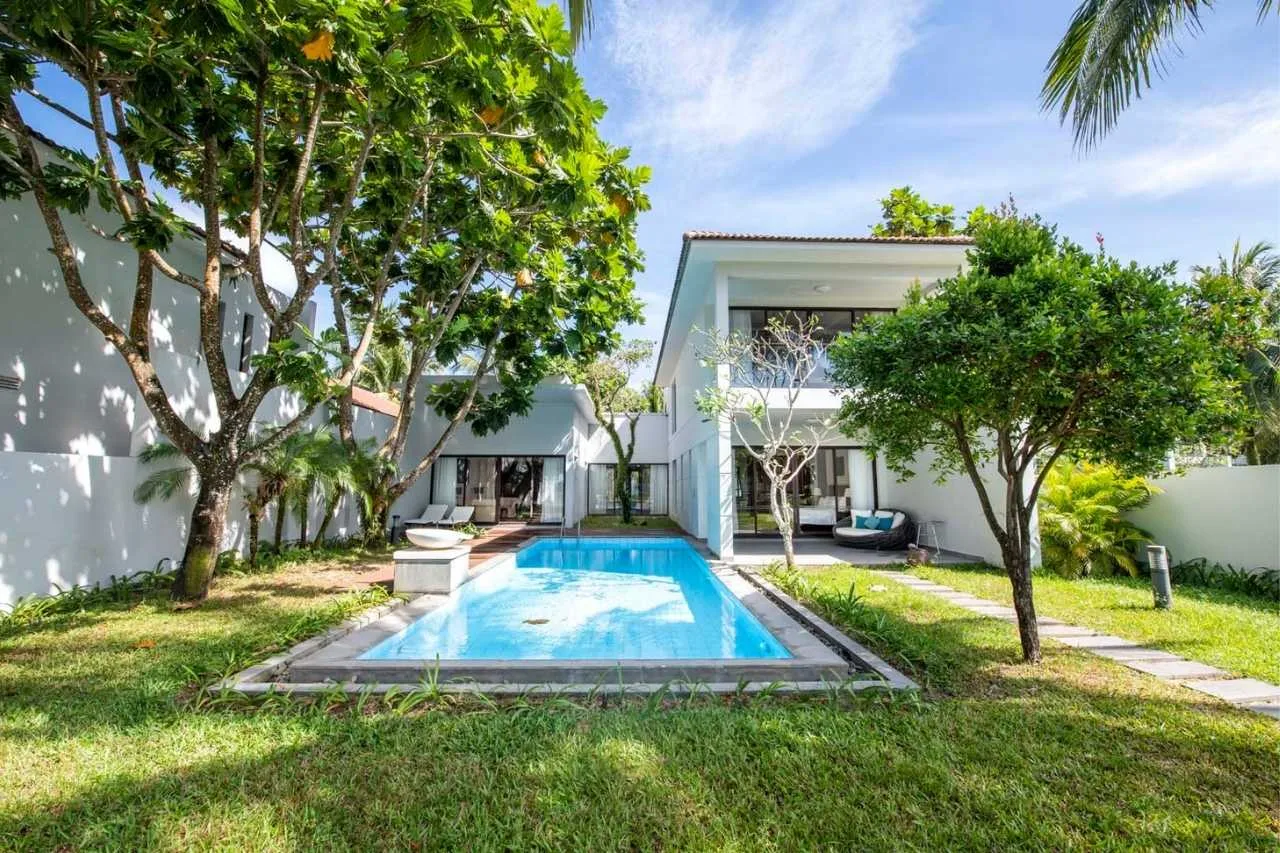 Biệt Thự 2 Phòng Ngủ Có Hồ Bơi Riêng tại Vinpearl Resort & Spa Phú Quốc: hồ bơi chữ nhật giữa bãi cỏ, hai tầng nhà trắng phía sau, cây xanh che bóng