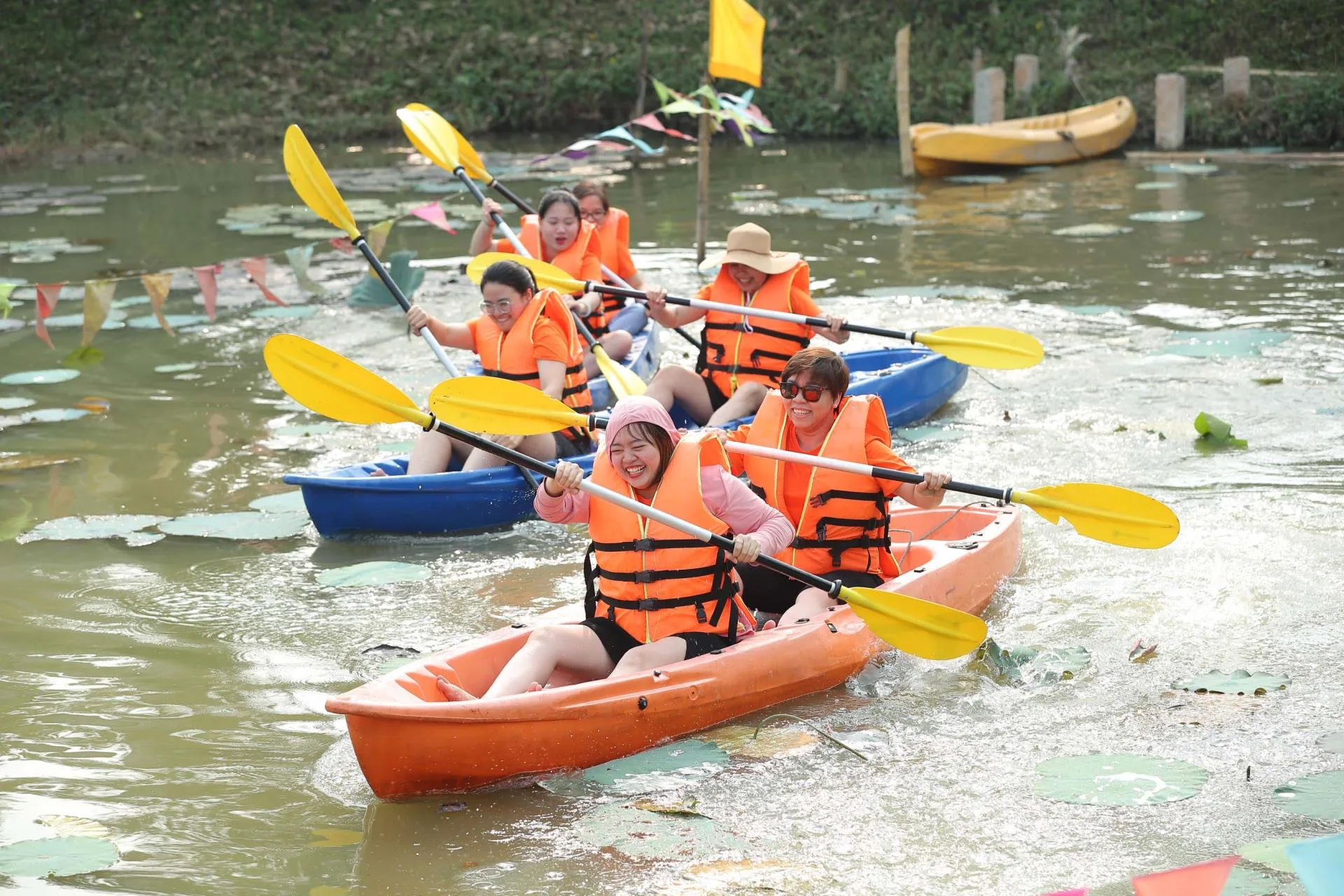Nhóm khách mặc áo phao cam chèo kayak đôi trên đầm sen ở Vườn Vua Resort & Villas