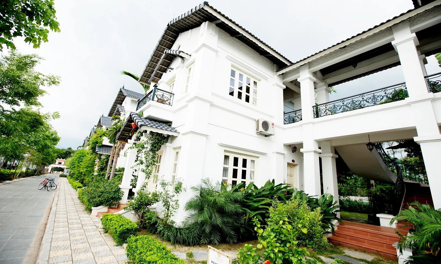 Dãy biệt thự Phố Tây trắng kiểu Pháp 2 tầng, ban công sắt uốn, cầu thang ngoài và xe đạp bên đường nội khu