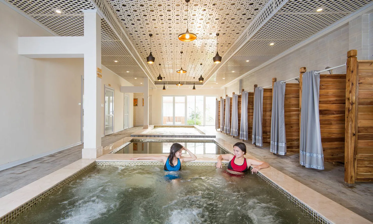 Khu tắm khoáng trong nhà ở Vườn Vua với các bể sục nối tiếp, trần chạm hoa văn và dãy buồng tắm vách gỗ rèm xám