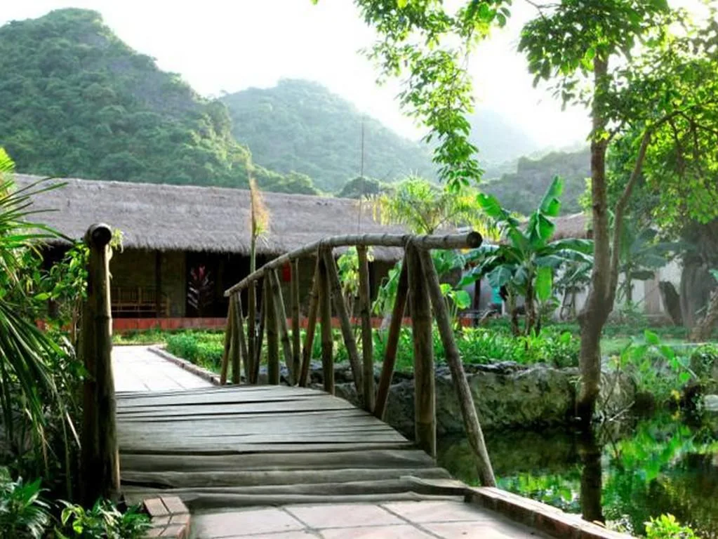 Cây cầu gỗ bắc qua lạch nước dẫn vào dãy bungalow mái lá dưới chân núi tại Whisper Nature Bungalow & Resort