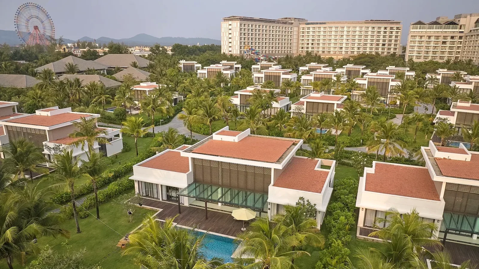 Khu villa mái ngói đỏ có hồ bơi riêng của Wyndham Grand Phu Quoc, phía sau là các tòa khách sạn, cầu trượt nước và vòng quay