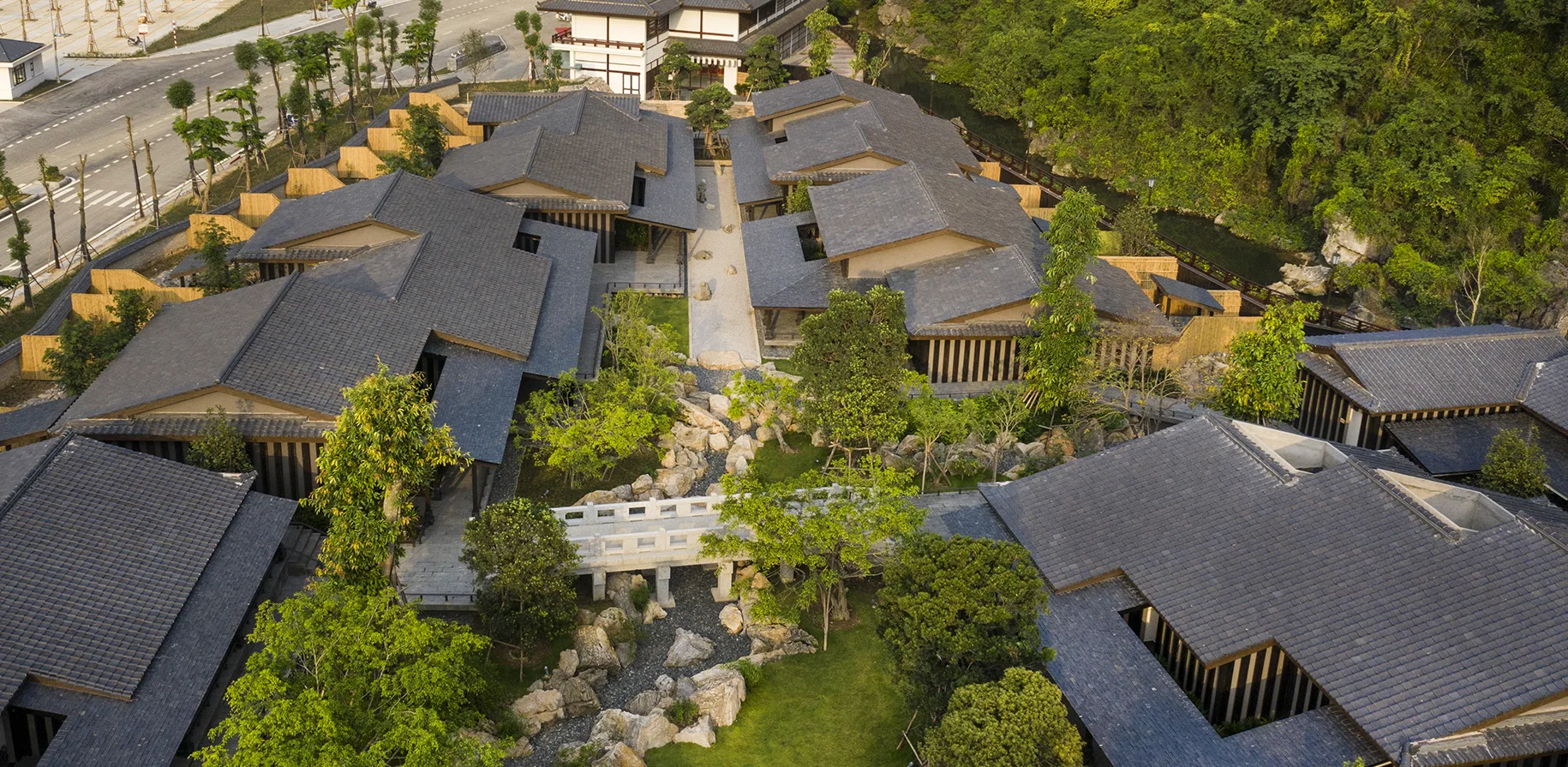 Yoko Onsen Quang Hanh nhìn từ trên cao, các dãy nhà mái xám kiểu Nhật quây quanh sân vườn đá và cầu nhỏ, sát chân núi phủ cây